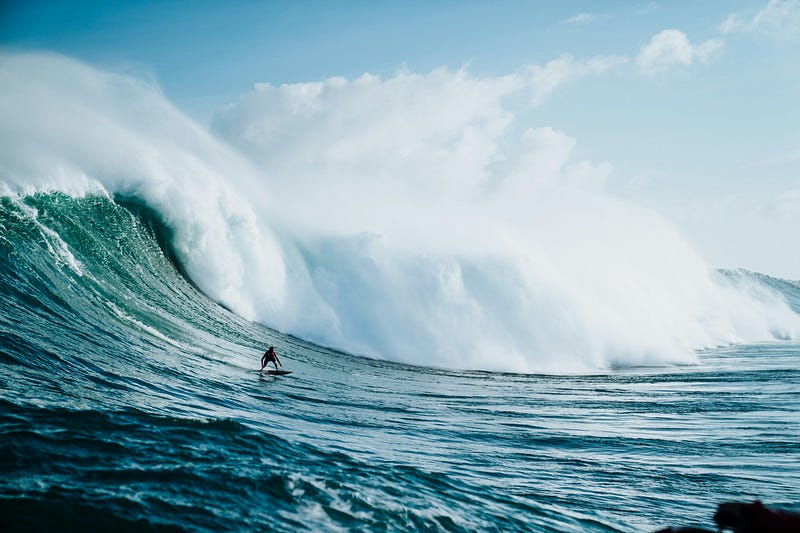 A man surfing through powerful ocean waves, balancing as the sea crashes around him, symbolising emotional resilience and freedom.